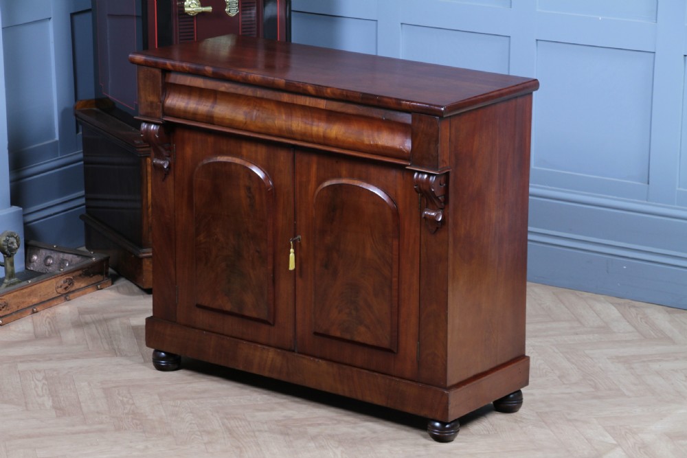 A Victorian flame mahogany two-door sideboard featuring a cushion drawer, arched panel doors, carved corbels, and turned bun feet. View II