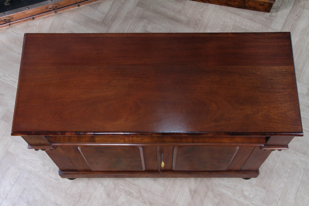 A Victorian flame mahogany two-door sideboard featuring a cushion drawer, arched panel doors, carved corbels, and turned bun feet. View VI