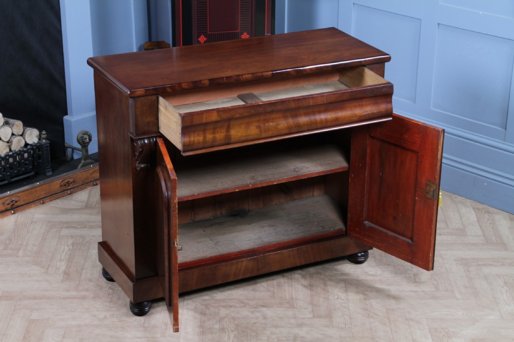 A Victorian flame mahogany two-door sideboard featuring a cushion drawer, arched panel doors, carved corbels, and turned bun feet. View VII