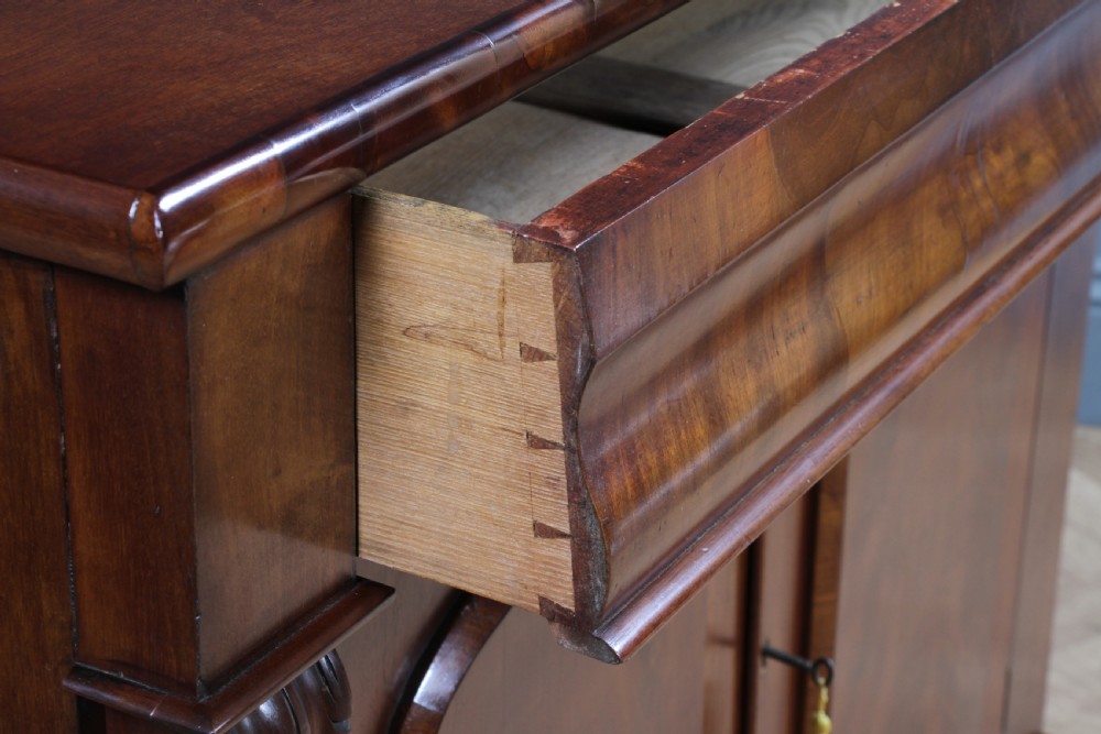 A Victorian flame mahogany two-door sideboard featuring a cushion drawer, arched panel doors, carved corbels, and turned bun feet. View X