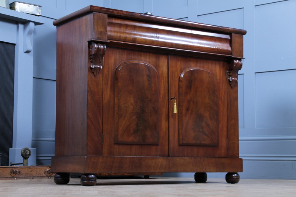 A Victorian flame mahogany two-door sideboard featuring a cushion drawer, arched panel doors, carved corbels, and turned bun feet. View XIII