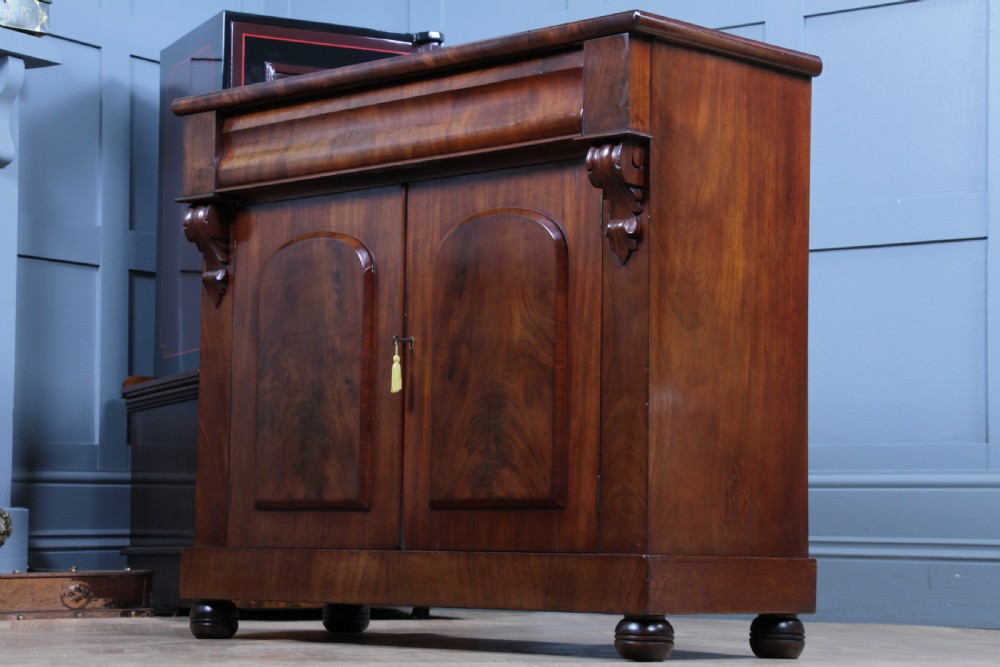 A Victorian flame mahogany two-door sideboard featuring a cushion drawer, arched panel doors, carved corbels, and turned bun feet. View XIV