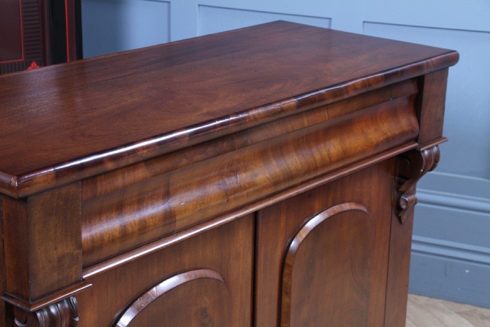 A Victorian flame mahogany two-door sideboard featuring a cushion drawer, arched panel doors, carved corbels, and turned bun feet. View XVI