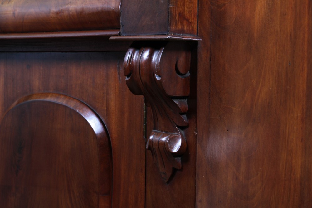 A Victorian flame mahogany two-door sideboard featuring a cushion drawer, arched panel doors, carved corbels, and turned bun feet. View XVII