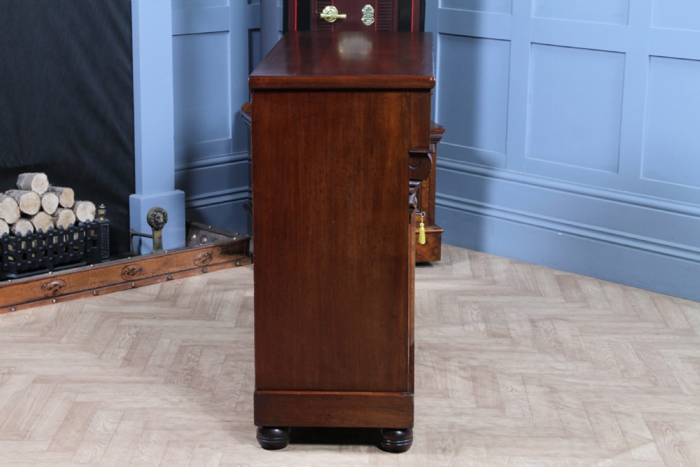 A Victorian flame mahogany two-door sideboard featuring a cushion drawer, arched panel doors, carved corbels, and turned bun feet. View XVIII