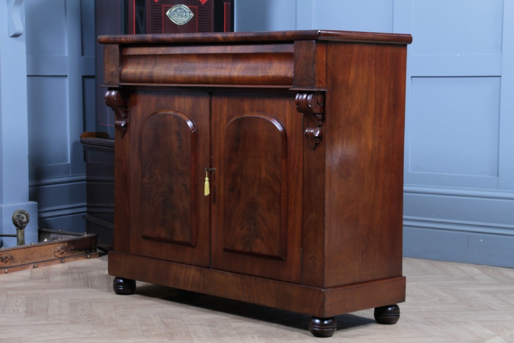 A Victorian flame mahogany two-door sideboard featuring a cushion drawer, arched panel doors, carved corbels, and turned bun feet. View XXIII