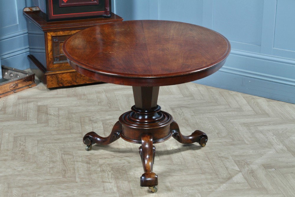 A Victorian oval mahogany tilt-top dining table supported by an octagonal column and a carved tripod base with brass castors. View V