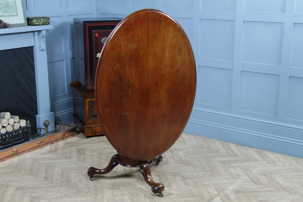 A Victorian oval mahogany tilt-top dining table supported by an octagonal column and a carved tripod base with brass castors. View VI