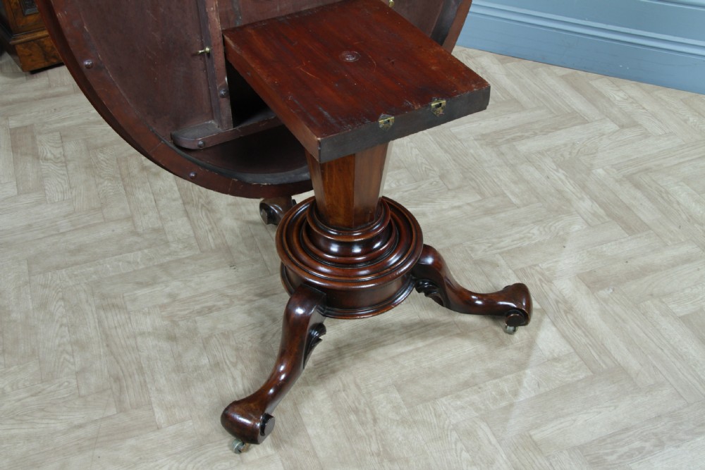 A Victorian oval mahogany tilt-top dining table supported by an octagonal column and a carved tripod base with brass castors. View VIII