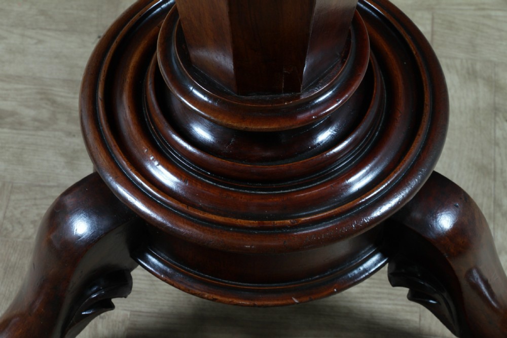 A Victorian oval mahogany tilt-top dining table supported by an octagonal column and a carved tripod base with brass castors. View XII