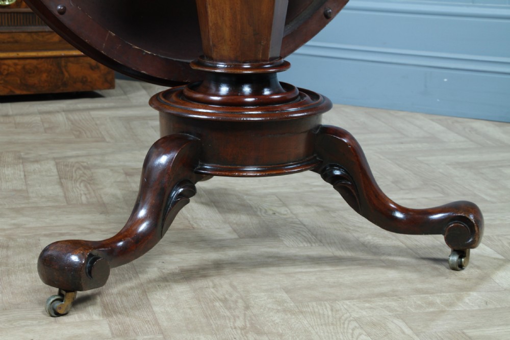 A Victorian oval mahogany tilt-top dining table supported by an octagonal column and a carved tripod base with brass castors. View XIV