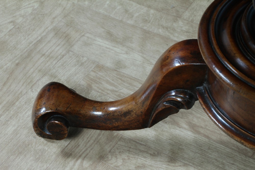 A Victorian oval mahogany tilt-top dining table supported by an octagonal column and a carved tripod base with brass castors. View XV