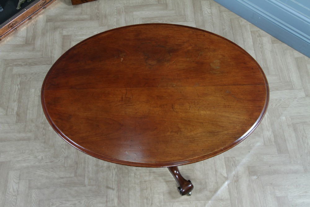 A Victorian oval mahogany tilt-top dining table supported by an octagonal column and a carved tripod base with brass castors. View XIX