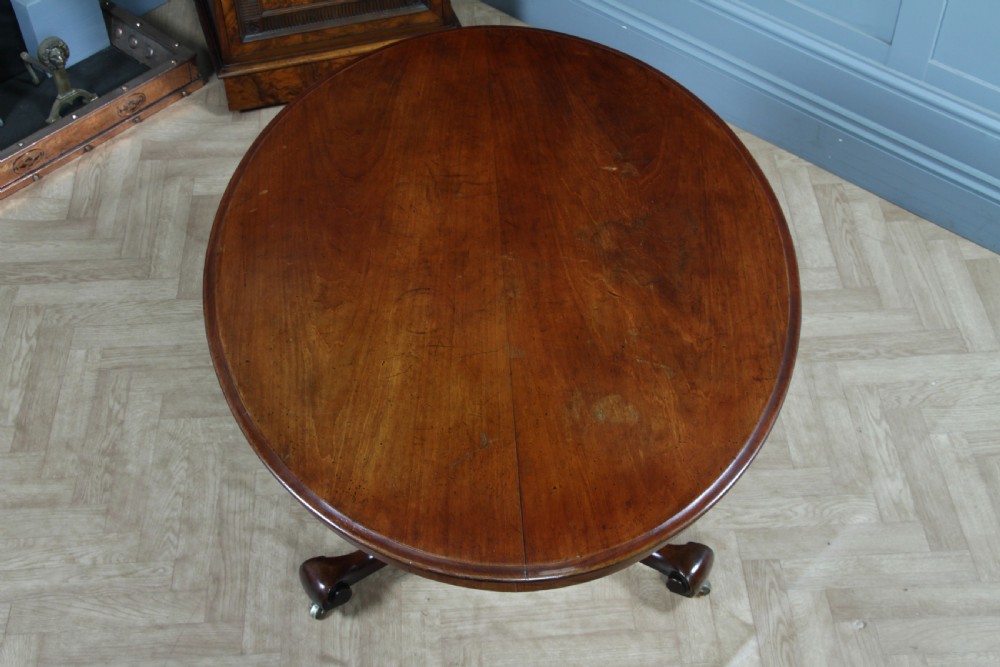 A Victorian oval mahogany tilt-top dining table supported by an octagonal column and a carved tripod base with brass castors. View XX