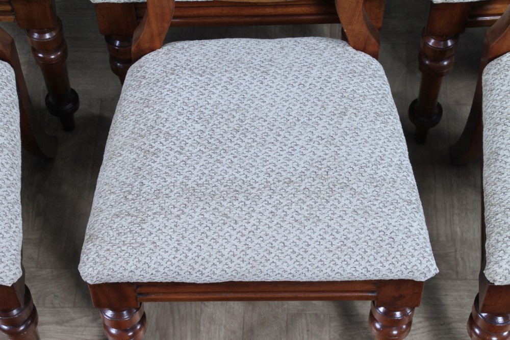 A set of eight Victorian mahogany dining chairs featuring open rounded balloon backs, turned front legs, and neutral patterned upholstered seats. View VI