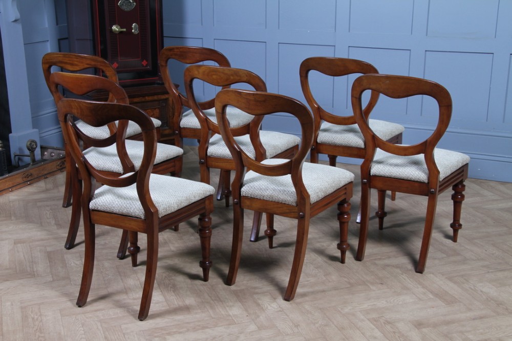 A set of eight Victorian mahogany dining chairs featuring open rounded balloon backs, turned front legs, and neutral patterned upholstered seats. View X