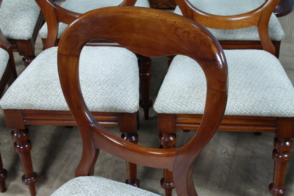 A set of eight Victorian mahogany dining chairs featuring open rounded balloon backs, turned front legs, and neutral patterned upholstered seats. View XV