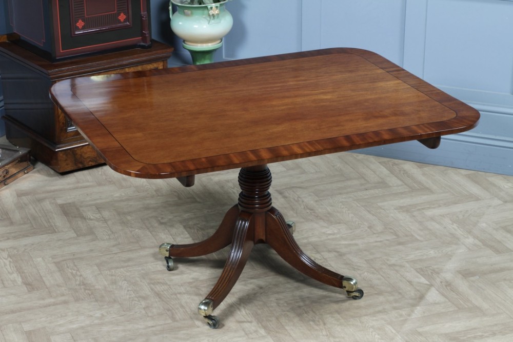 A Regency mahogany tilt-top dining table featuring a rectangular crossbanded top supported by a turned pedestal column and four reeded sabre legs with brass castors.