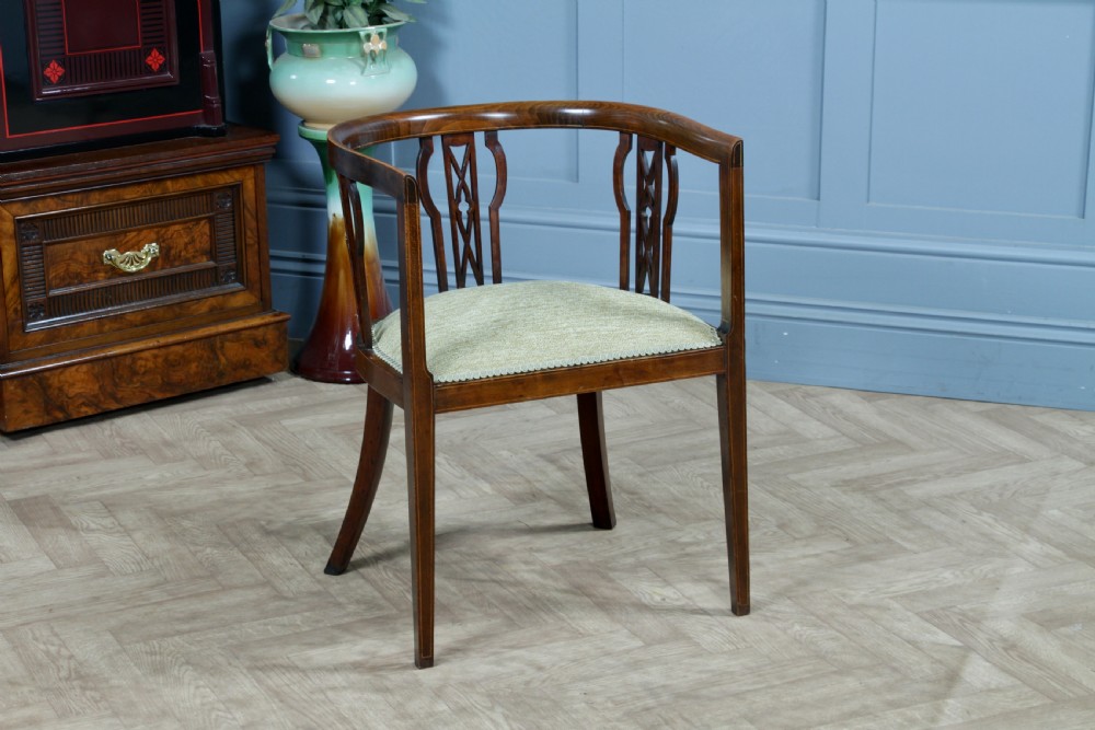 An Edwardian inlaid mahogany tub armchair featuring a continuous curved backrest, pierced splats, and a sage green upholstered seat.