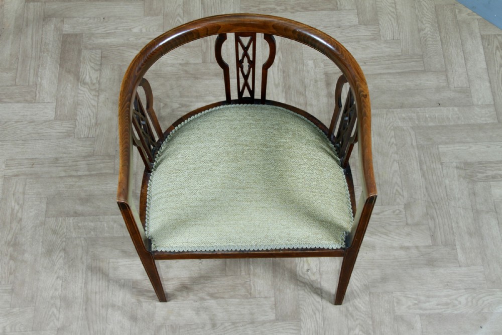 An Edwardian inlaid mahogany tub armchair featuring a continuous curved backrest, pierced splats, and a sage green upholstered seat. View IV