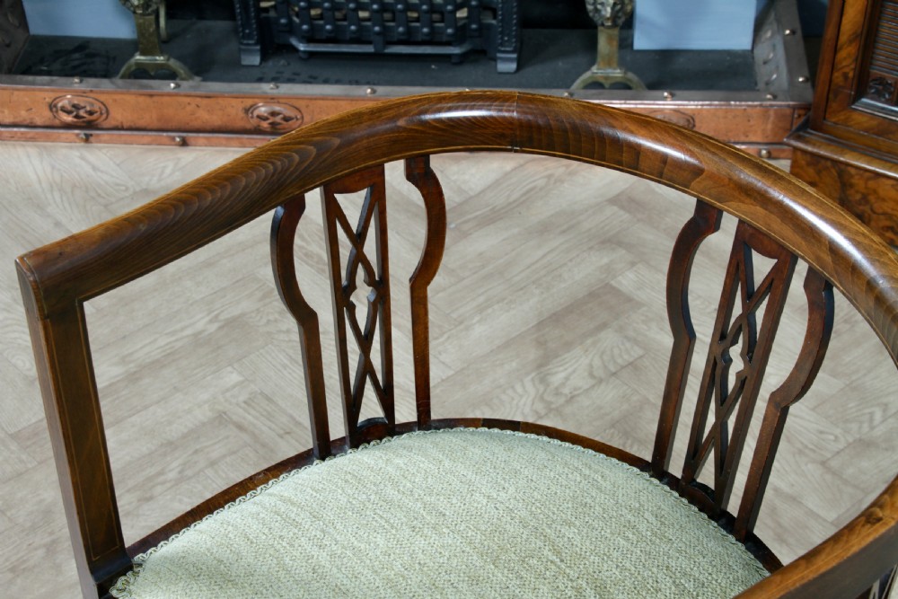 An Edwardian inlaid mahogany tub armchair featuring a continuous curved backrest, pierced splats, and a sage green upholstered seat. View X