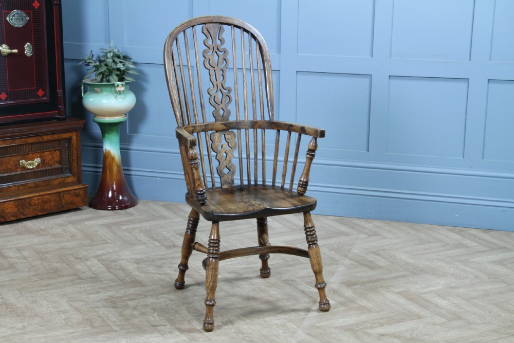 A traditional high-back Windsor armchair crafted from ash and elm wood, featuring a pierced central splat, spindled backrest, turned legs, and a cow horn stretcher.