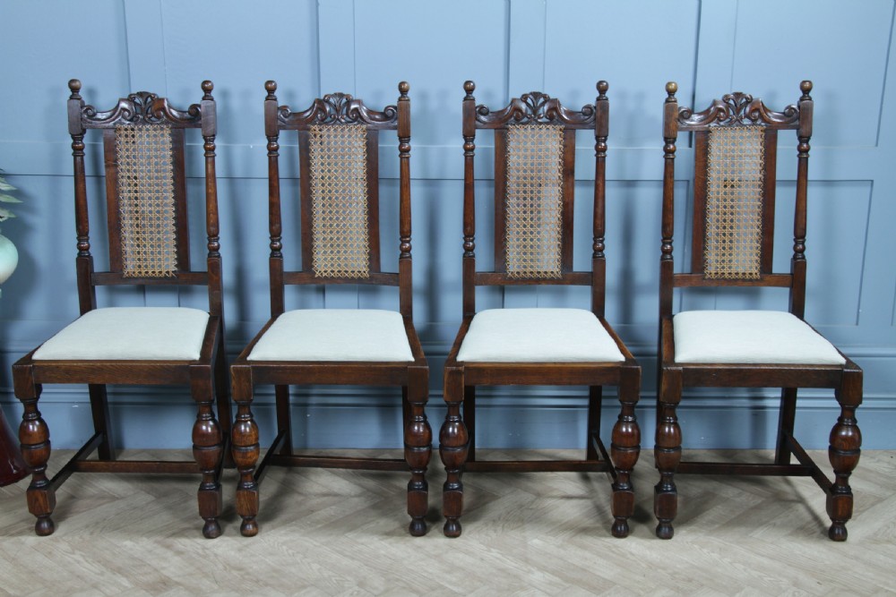 A set of four dark oak Jacobean Revival dining chairs featuring woven cane backs, carved crests, turned legs, and cream fabric seats. View III