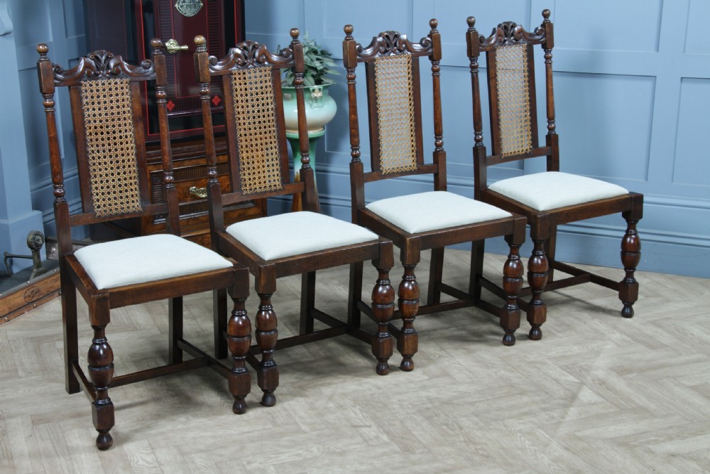 A set of four dark oak Jacobean Revival dining chairs featuring woven cane backs, carved crests, turned legs, and cream fabric seats. View XII