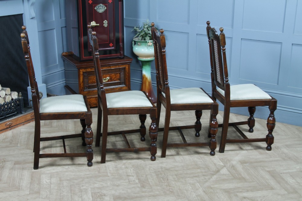 A set of four dark oak Jacobean Revival dining chairs featuring woven cane backs, carved crests, turned legs, and cream fabric seats. View XIV