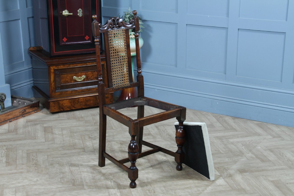A set of four dark oak Jacobean Revival dining chairs featuring woven cane backs, carved crests, turned legs, and cream fabric seats. View XX