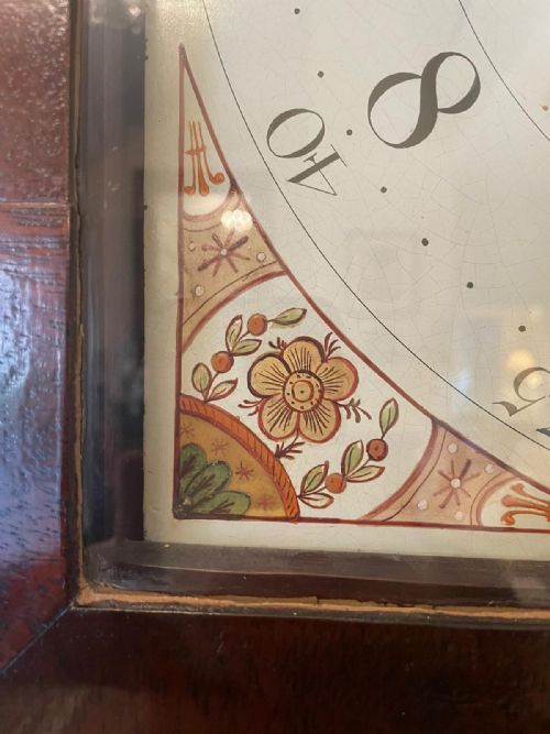 fig 1. A George III mahogany longcase clock featuring a swan neck pediment with a brass finial, a painted arch dial, and an inlaid trunk door.