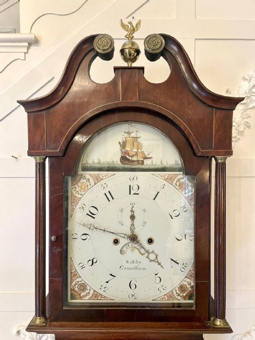 fig 2. A George III mahogany longcase clock featuring a swan neck pediment with a brass finial, a painted arch dial, and an inlaid trunk door.