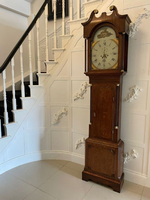 fig 1. A George III oak longcase clock featuring a swan-neck pediment hood, an arched painted dial displaying Roman numerals, and fluted quarter columns.