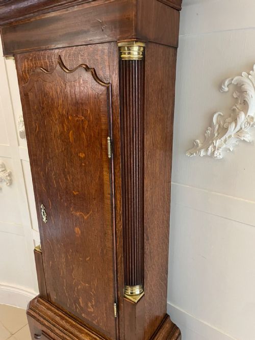 fig 2. A George III oak longcase clock featuring a swan-neck pediment hood, an arched painted dial displaying Roman numerals, and fluted quarter columns.
