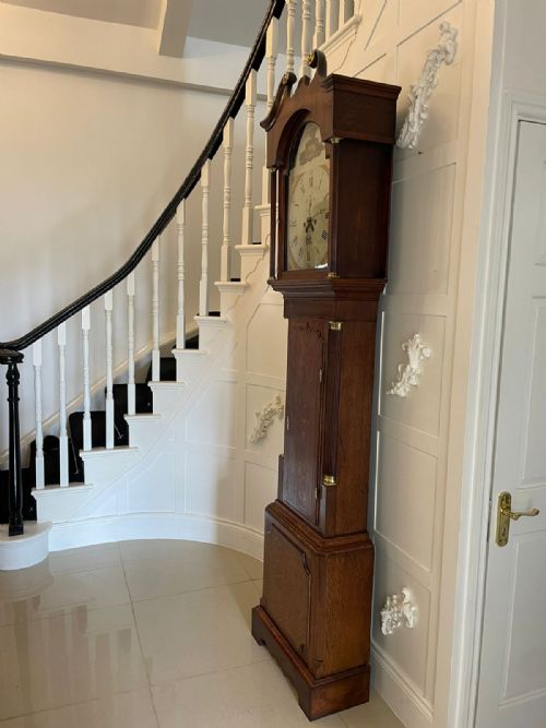fig 3. A George III oak longcase clock featuring a swan-neck pediment hood, an arched painted dial displaying Roman numerals, and fluted quarter columns.