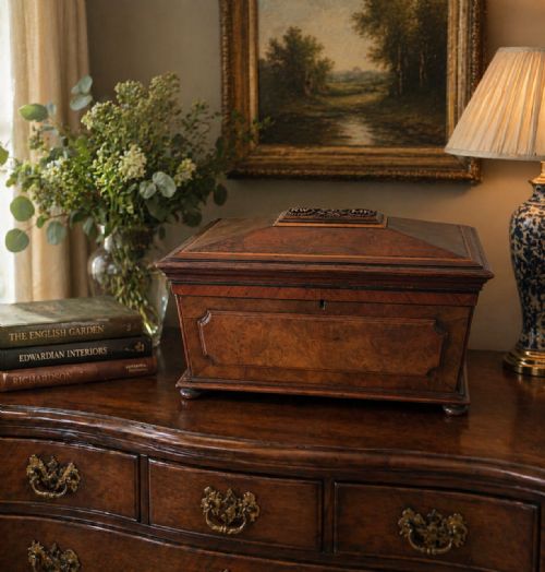 fig 1. A Victorian burr walnut sarcophagus-shaped tea caddy featuring a carved top plaque, stepped lid, keyhole escutcheon, and small bun feet.