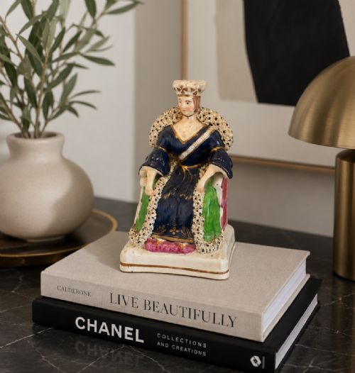 fig 1. An antique Staffordshire earthenware flatback figure depicting a seated Queen Victoria wearing a crown and cobalt blue gown with gilded accents.