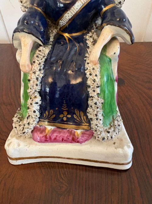 fig 2. An antique Staffordshire earthenware flatback figure depicting a seated Queen Victoria wearing a crown and cobalt blue gown with gilded accents.