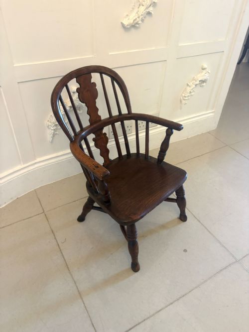 fig 1. An antique Georgian childs Windsor armchair made of dark brown elm wood featuring a shaped back splat and turned legs.
