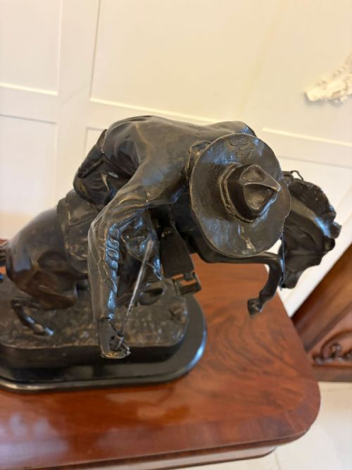 fig 2. A dark patinated bronze sculpture depicting a cowboy wearing a hat atop a bucking horse on an oval base.