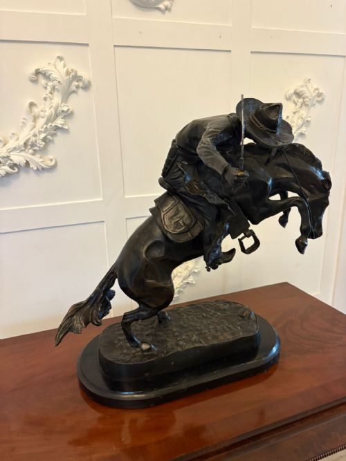 fig 3. A dark patinated bronze sculpture depicting a cowboy wearing a hat atop a bucking horse on an oval base.