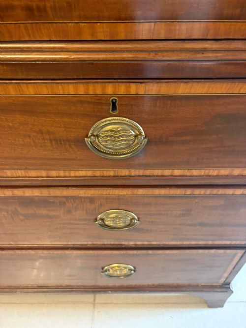 fig 2. An antique Georgian mahogany linen press featuring oval satinwood inlay motifs on two upper doors above four drawers with brass handles.