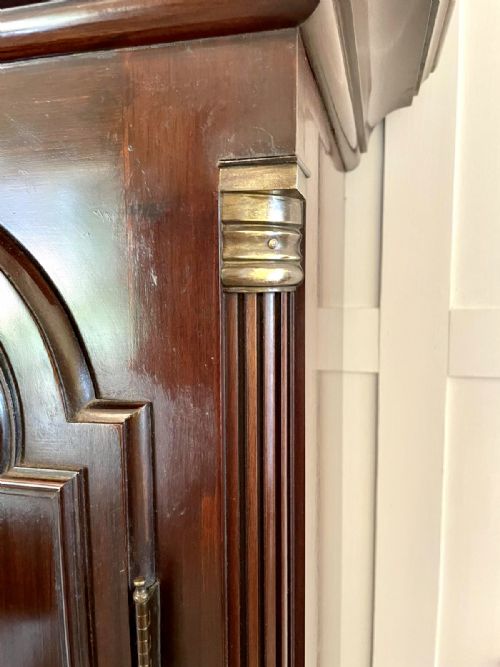 fig 3. An antique Victorian dark mahogany longcase clock with a swan-neck pediment, ornate brass dial, arched trunk door, and stepped base.