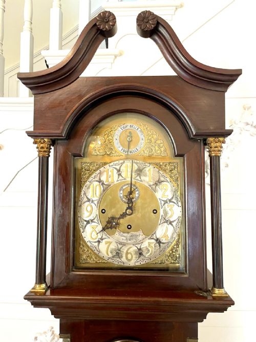 fig 5. An antique Victorian dark mahogany longcase clock with a swan-neck pediment, ornate brass dial, arched trunk door, and stepped base.