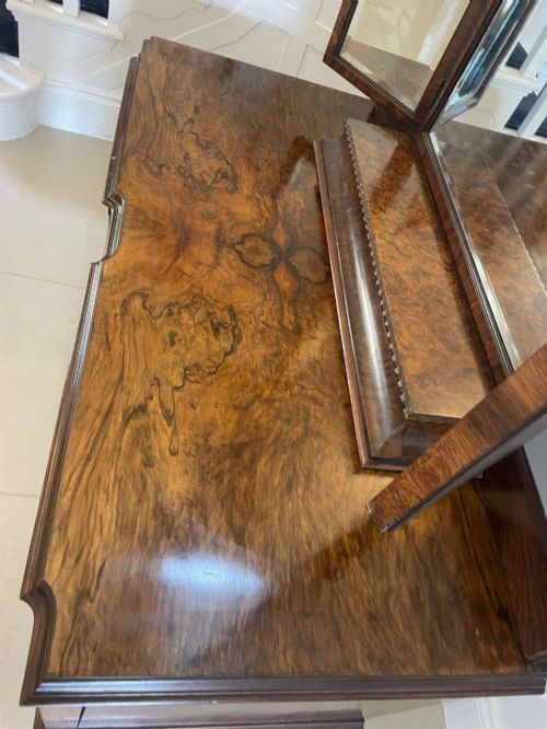 fig 1. A burr walnut dressing table featuring a central arched triptych mirror, highly figured wood grain, and six drawers with ornate brass handles.