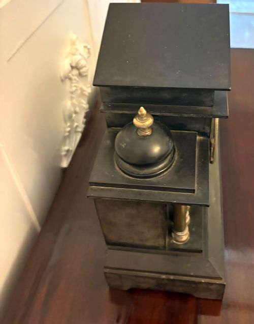 fig 4. An architectural black marble mantel clock featuring gilt brass columns, a relief frieze panel depicting classical figures, and a round dial with Arabic numerals.