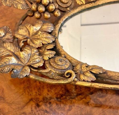 fig 1. An oval gilt metal tray featuring a central mirror panel surrounded by an ornate border of sculpted grapevines, leaves, and grape clusters.