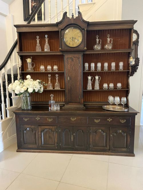 fig 1. An eighteenth-century dark oak George III dresser featuring an upper shelf rack with an integrated central longcase clock over a base with three drawers and six arched panel cupboard doors.