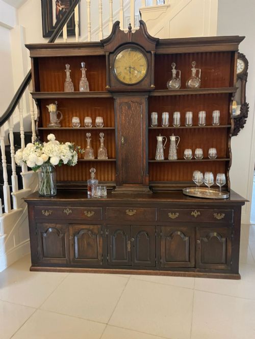 fig 2. An eighteenth-century dark oak George III dresser featuring an upper shelf rack with an integrated central longcase clock over a base with three drawers and six arched panel cupboard doors.