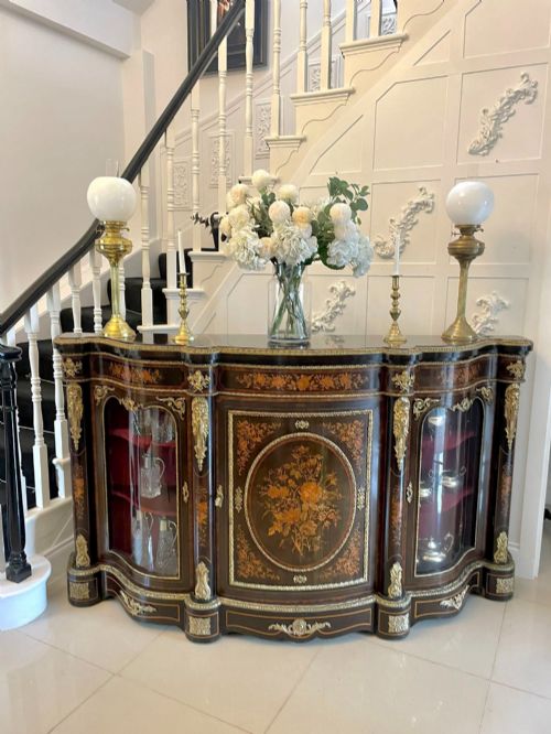 fig 1. A dark wood Victorian serpentine credenza with floral marquetry inlay, gilt ormolu mounts, and two curved glass display doors.